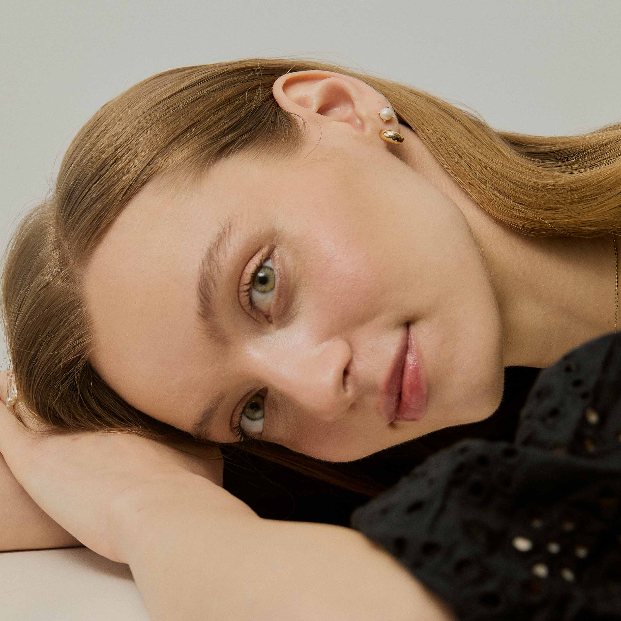 Model purtând cerceii Gold Drop din aur 14K, evidențiind modul în care designul fluid reflectă lumina pe lobul urechii.